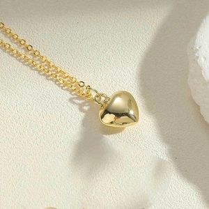 Macro shot of 3D gold heart pendant with mirror polish finish on a textured background