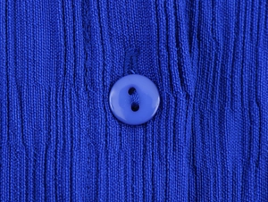 Makroaufnahme der vertikalen Rippstrick-Struktur und passendem blauem Knopf am Kleid