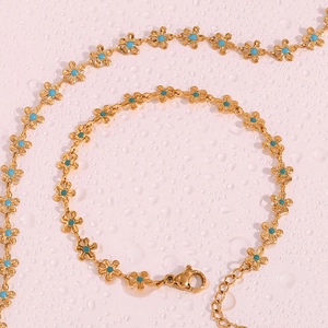 Close-up of gold flower necklace with turquoise inlay and lobster clasp on pink background