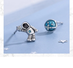 Macro shot of asymmetrical silver astronaut and blue planet stud earrings with zircon