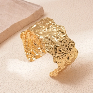 Detailed macro view showing the irregular textured gold pleated surface of the metal cuff