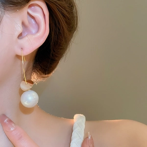 Detailed close-up of a large white pearl drop earring with a golden hook on a model