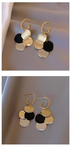 Detailed view of long tassel earrings with contrasting gold and black metal discs