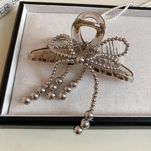 Detail of acrylic bow hair claw with silver beaded tassels on a jewelry tray