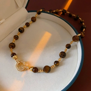 Dettaglio macro della collana con occhio di tigre e chiusura ad anello in oro e strass