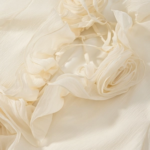 Detailed macro view of handmade 3D floral accents and ruffled pleats on cream dress
