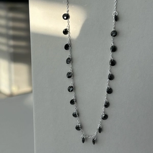 Detail of silver chain necklace with faceted black teardrop and round gemstones