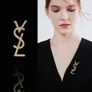 Close-up of a gold-tone YSL heart brooch with crystal inlays and tassel on a model
