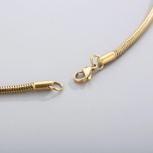 Detail of a golden lobster clasp on a sleek titanium steel round snake chain necklace