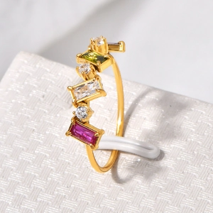 Gros plan d'une bague dorée avec pierres multicolores sur un support de présentation blanc