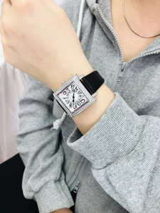 Detalle de un reloj cuadrado con diamantes, números grandes y correa de cuero negro