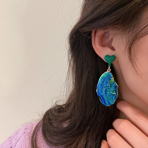 Close-up of model wearing heart-shaped green and blue resin earrings with gold edges