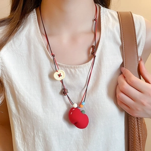 Detail of fabric beaded necklace with red heart pendant and apple charm on model