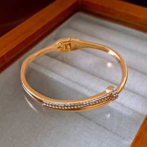 Detailed view of a gold nail bracelet with micro-pave crystals on a grey velvet tray