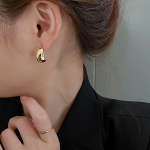 Close-up of a model wearing minimalist golden pea-shaped stud earrings with glossy finish