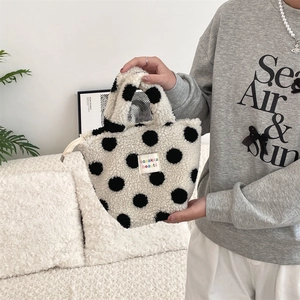 Detail of plush polka dot handbag with zipper closure and brand label on fluffy fabric