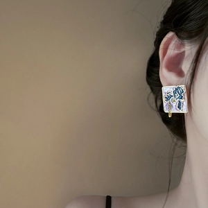 Detailed view of a gold-framed square earring with hand-painted blue iris flowers
