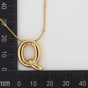 Detailed view of puffed gold letter Q pendant on a scale showing 22mm height size