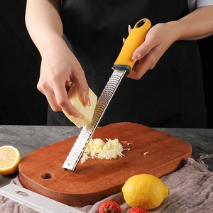 Stainless steel cheese grater with yellow handle used on lemon over wooden board