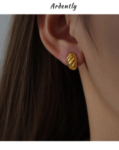 Macro shot of gold-plated twisted C-shaped earrings worn to show texture and scale