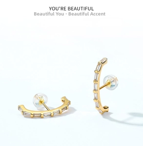 Macro view of gold C-shape earrings with baguette-cut zircons and silicone backs