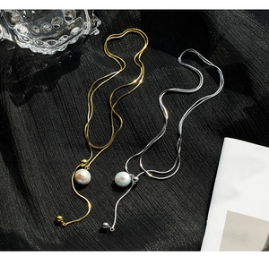 Detail of silver and gold Y-shaped sweater necklaces with baroque pearls on black silk fabric