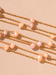 Macro shot of gold chain necklace with irregular pink freshwater pearls on beige texture