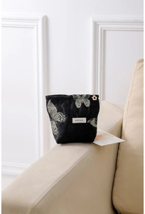 Detail of a black velvet makeup bag featuring golden butterfly patterns and a floral zipper