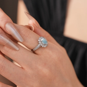 Close-up of elegant silver ring with oval blue gemstone and zircon floral halo on finger