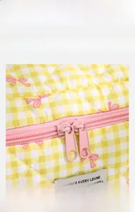 Detail of smooth pink metal dual zippers on a quilted yellow plaid makeup bag