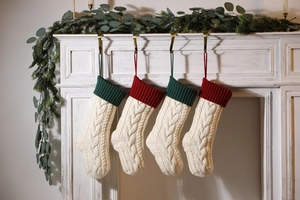 Detail of cable knit Christmas stockings in ivory, red and green hanging on a white fireplace
