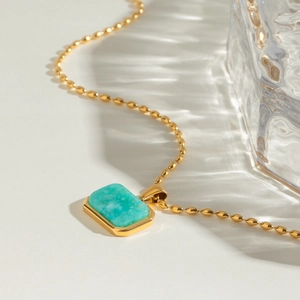 Detailed macro view of 18k gold beaded chain and rectangular green gemstone pendant