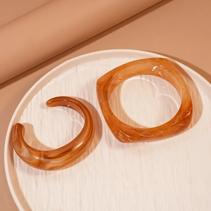 Set aus bernsteinfarbenem Harzarmreif und quadratischem Armband auf Keramikschale