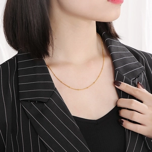 Collier minimaliste en acier inoxydable doré porté sur une veste noire à rayures