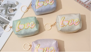 Close-up of sparkling sequin coin purses in silver, gold and green with love embroidery