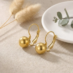 Close-up of polished gold steel ball leverback earrings on a textured fabric background