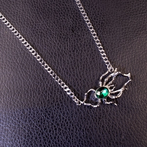 Detailed macro view of a silver spider pendant with an oval emerald-green gemstone inlay