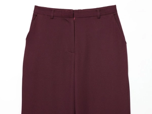 Detail of burgundy suit trousers showing waistline and pocket construction on white background