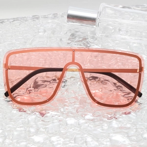Pink oversized one-piece sunglasses with transparent frames on a rippled glass surface