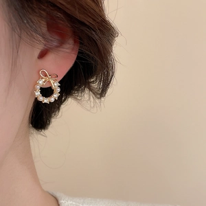 Close-up of elegant gold wreath earring with bow knot, pearls and crystals on ear