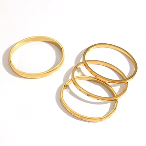 Set of five gold stainless steel bangles with sparkling zircon accents on white background
