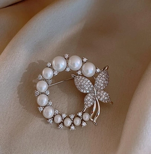 Detail der eleganten Perlenkranz-Brosche mit funkelndem Zirkonia-Schmetterling auf Seide