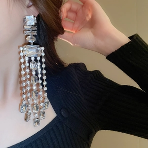 Macro shot of sparkling silver tassel earrings featuring crystals on a black knit collar