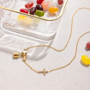 Détail des pendentifs croix, clé et cadenas dorés sur un collier en acier inoxydable