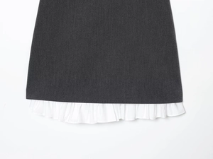 Close-up of dark grey woven fabric with white ruffled hem detail on dress