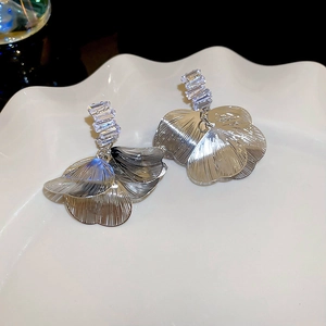 Close-up of silver zircon petal earrings on a white ceramic tray with brushed metal details