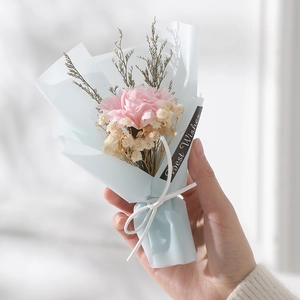 Close-up of a small handmade pink carnation and dried flower bouquet with blue wrapping