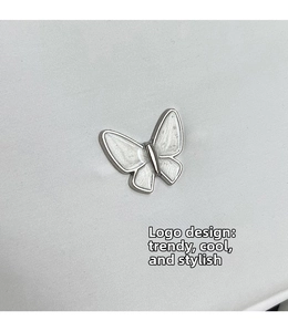 Detailed view of butterfly-shaped enamel accessory with silver frame on white fabric