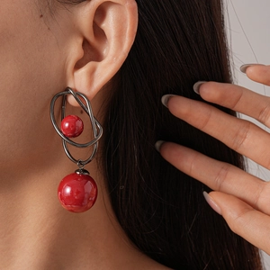 Close-up of geometric acrylic hoop earring with a red bead on female model