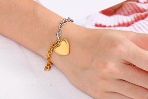 Detail of mixed-metal link bracelet with gold heart pendant worn on a female wrist